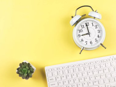 Üst görünüm ya da düz bilgisayar klavyesi, beyaz klasik alarm saati 9 o 'clcock ve sulu saksıyı sarı arkaplanda metin için kopyalama alanı ile birlikte gösteriyor. Sabah rutini.