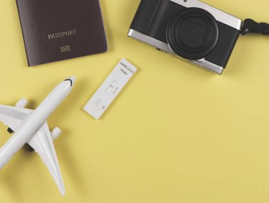 Covid-19 negatif test sonuçları antijen test kiti (ATK), kamera, uçak modeli ve sarı zemin üzerinde fotokopi alanı olan pasaport. Yeni normal seyahat .