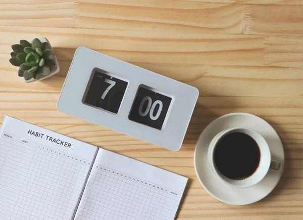 Top view or flat lay of habit tracker book, a cup of black coffee, flip clock 7 am and succulent plant pot on wooden table background with copy space. self development concept.