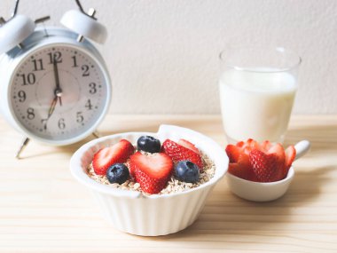 Kahvaltı seti, yulaf ya da tahıl gevreği, taze yaban mersini ve çilek, bir bardak süt ve saat 7 'de çalacak. Tahta masada. Sağlıklı kahvaltı kavramı.