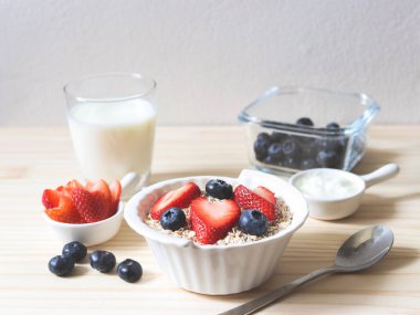 Beyaz kâse, kaşık, taze yaban mersini, çilek, bir bardak süt ve yulaf ezmeli kahvaltı manzarası. Sağlıklı kahvaltı kavramı.