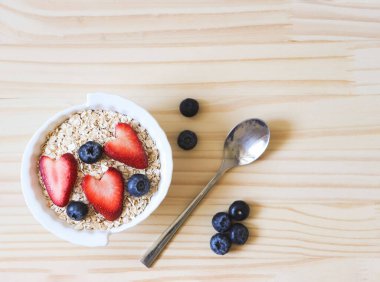 Beyaz kâse, kaşık, taze yaban mersini, çilek, bir bardak süt ve yulaf ezmeli veya tahıllı kahvaltı. Sağlıklı kahvaltı kavramı.