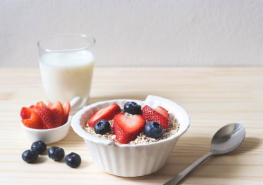 Kahvaltıda yulaf, tahıl gevreği, taze yaban mersini, çilek ve bir bardak süt. Sağlıklı kahvaltı kavramı.