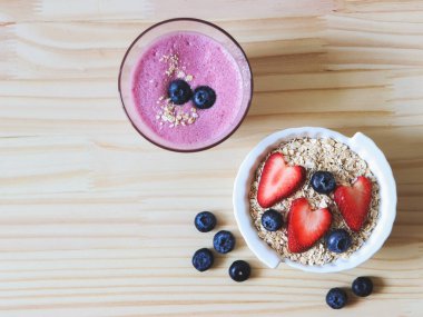 Üst ya da düz kahvaltı, yulaf ezmesi ya da tahıl gevreği, taze yaban mersini, çilek, ahşap masada bir bardak yabanmersini püresi. Sağlıklı kahvaltı kavramı.
