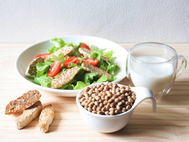 Front view of soy bean seeds in white bowl, tempeh in salad dish and soy milk on wooden table, products of soy beans.
