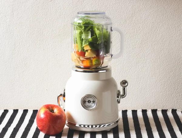 Front view of  white vintage blender or smoothie maker machine  with an apple on  black and white stripe table cloth and white wall. Healthy drink making.