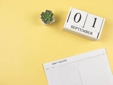 Top view or flat lay of habit tracker book with with  succulent plant pot and wooden calendar 01 september on yellow background. 