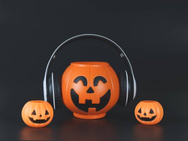 Kulaklıklı büyük plastik cadılar bayramı balkabağı kabağı örtüsü, siyah arka planda küçük balkabaklarıyla izole edilmiş, kopyalama alanı. Cadılar Bayramı müziği veya podcast.