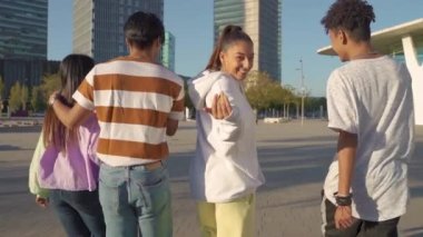 Çok ırklı, mutlu bir grup genç arkadaş sokakta yürüyorlar ve kameraya davet ediliyorlar..