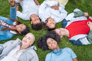 Çoklu etnik eğilimli genç arkadaşların parkın çimlerinde daireler çizerek gülümsemelerinin üst açısı..