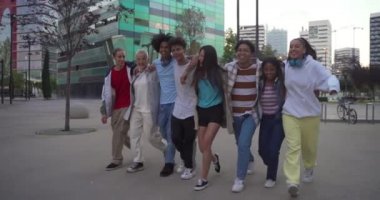 Çok ırklı, mutlu genç arkadaşlar sokakta yürürken ve zıplarken birbirlerine sevgiyle sarılıyorlar..