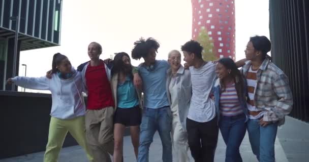 Fiatal, boldog barátok soknemzetiségű csoportja sétál és ugrál az utcán, szeretetteljesen ölelve egymást.. — Stock videók