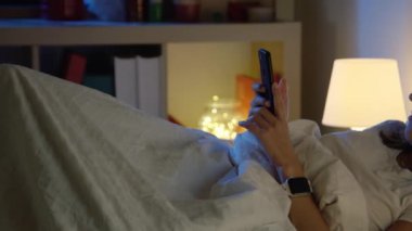 Güzel genç kız gecenin bir yarısı telefonunu yatakta arıyor. Yatak konseptinde teknoloji. 4K Kırmızı Kamera.