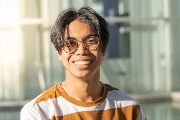 Portrait of a handsome asian young man smiling and looking at camera outdoors in the student campus during a sunny day. — 图库照片