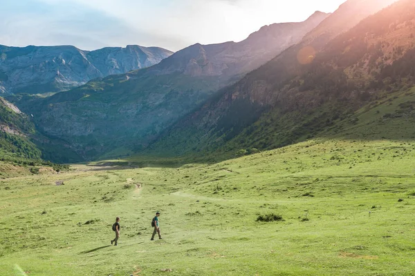 Jonge paren wandelen in een prachtig dal tussen bergen tijdens de zonsondergang. Ontdekking Reisbestemming Concept. — Stockfoto