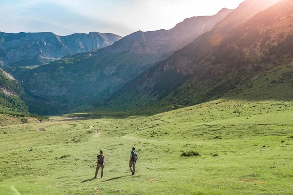 Jonge paren wandelen in een prachtig dal tussen bergen tijdens de zonsondergang. Ontdekking Reisbestemming Concept. — Stockfoto