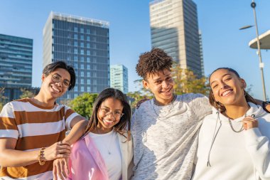 Çok ırklı, neşeli gençler sokakta kameraya bakıp gülüp sarılıyorlar..