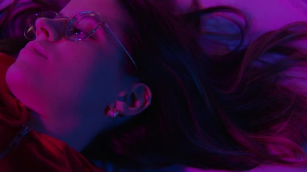 Top view of a beautiful girl sleeping cozily on a bed in her night room with colorful pink neon lights. — Stock Video