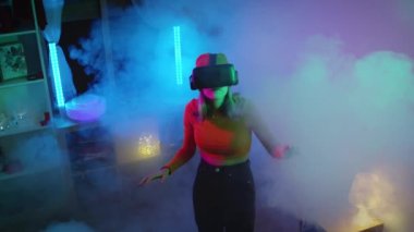  Karanlık odada, neon ışıklı 4K yavaş çekim RED kameralı sanal gerçeklik gözlüğü kullanan genç bir kadın. Kablosuz teknolojiler.