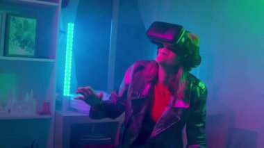  Karanlık odada, neon ışıklı 4K yavaş çekim RED kameralı sanal gerçeklik gözlüğü kullanan genç bir kadın. Kablosuz teknolojiler.