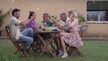 Mutlu arkadaşlar büyük bir gülümsemeyle gülüyor ve bir yaz lokantasında kadeh kaldırıyorlar. Ev verandasında yemek yerken gülümseyen insanlar. Gülümseme, neşe konsepti. Yüksek kalite 4k görüntü