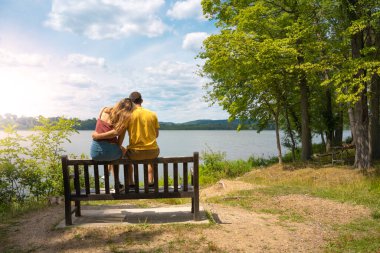 Young loving couple cuddled together on a bench in a lake in summer. High quality photo