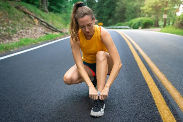 Female athlete tying laces for jogging run on forest road. Runner woman getting ready for training exercise. Motivation health and fitness exercise. Sport lifestyle concept. Copy space banner. High