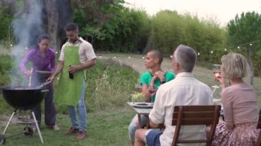 Happy friends laughing and toasting with a big smile around the barbecue. Smiling people eating at the barbecue on the patio of the house in the summer. Joy concept. High quality photo