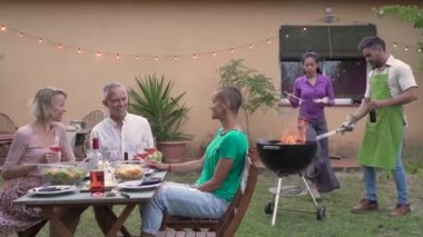 Çok ırklı arkadaşlar barbekü yapar. Yazın terasta yemek yiyen gülümseyen insanlar. Eğlence konsepti. Yüksek kalite 4k görüntü