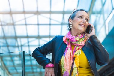Akıllı telefonuyla konuşan olgun çekici bir kadın mutlu bir şekilde gülümsüyor. Teknoloji konsepti. Yüksek kalite fotoğraf