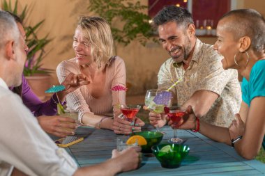 Bir grup çok kültürlü neşeli arkadaş gece partisinde kokteyl içiyor ve birlikte eğleniyorlar. Gece içkilerinin tadını çıkarıyorum. Yüksek kalite fotoğraf