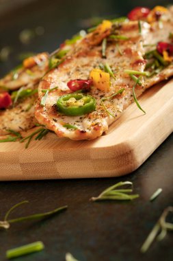 Macro close-up of grilled chicken breast cooked with three different colors chili peppers and aromatic herbs.