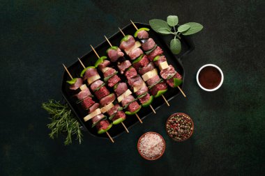 Raw meat skewers before cooking on a dark background.