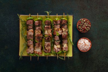Baked meat skewers on a green dish with salt and mixed pepper. 