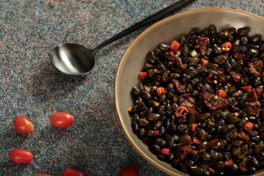 Black beans with dried tomatoes and red Cayenne chili peppers in a brown dish.
