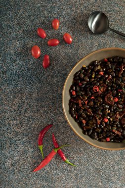 Black beans with dried tomatoes and red Cayenne chili peppers in a brown dish.