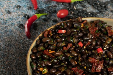 Macro close up of black beans with dried tomatoes and red Cayenne chili peppers in a brown dish.