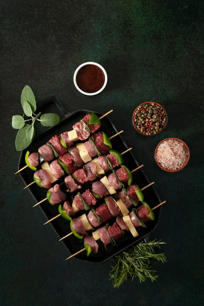 Raw meat skewers before cooking on a dark background.