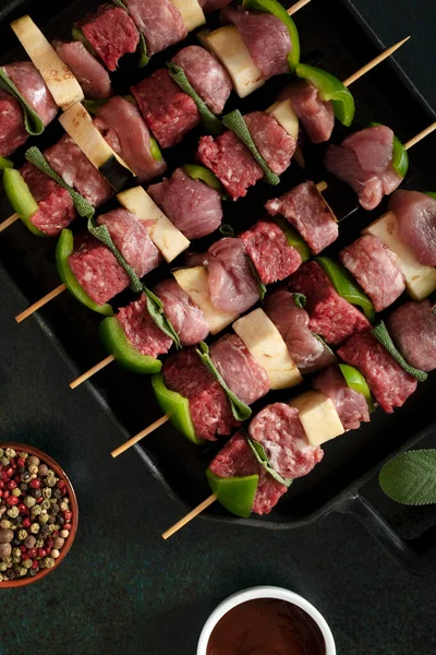 Raw meat skewers before cooking on a dark background.