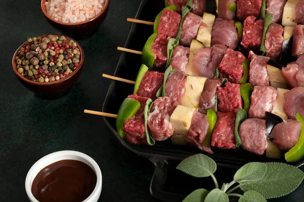 Raw meat skewers before cooking on a dark background.