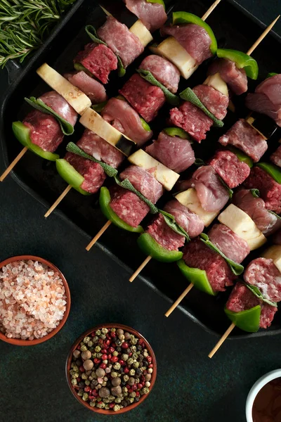 Raw meat skewers before cooking on a dark background.