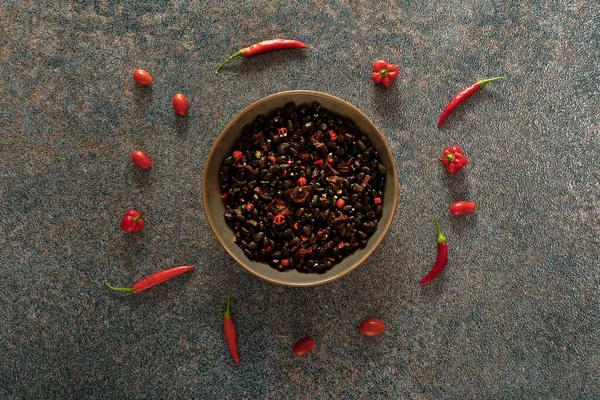 Black beans with dried tomatoes and red Cayenne chili peppers in a brown dish.