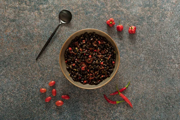 Black beans with dried tomatoes and red Cayenne chili peppers in a brown dish.