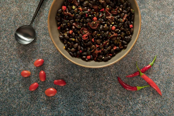 Black beans with dried tomatoes and red Cayenne chili peppers in a brown dish.