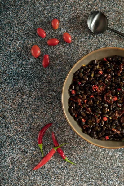 Black beans with dried tomatoes and red Cayenne chili peppers in a brown dish.