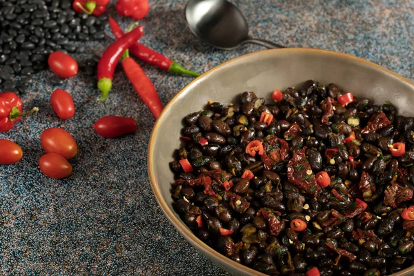 Black beans with dried tomatoes and red Cayenne chili peppers in a brown dish.