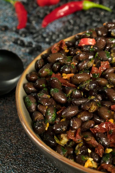 Macro close up of black beans with dried tomatoes and red Cayenne chili peppers in a brown dish.