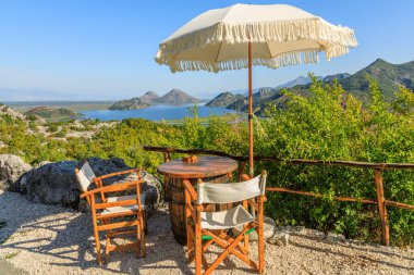 Skadar Gölü 'ne panoramik manzara ve Karadağ' daki karayolu kafesinden masa, sandalye ve şemsiyeli dağlar