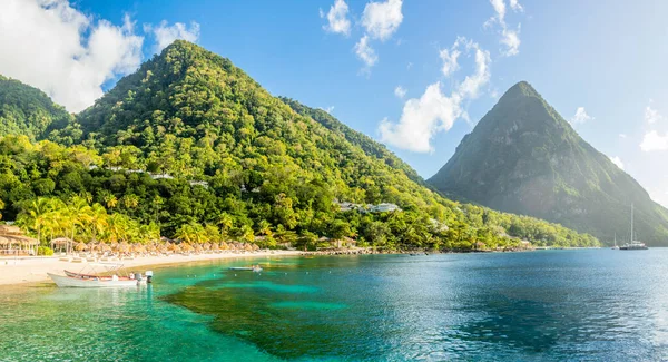 Arka planda Gros Piton Dağı, Sugar Sahili, Saint Lucia ile kıyıda palmiyeler ve saman umrellaları olan Karayipler plajı