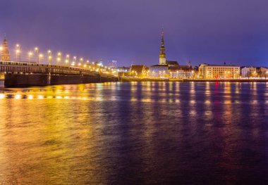 Gece görüşü tarihi şehir merkezine ve Daugava nehrinin kıyısındaki taştan köprüye sokak lambalarıyla renklendirilmiş Riga, Letonya